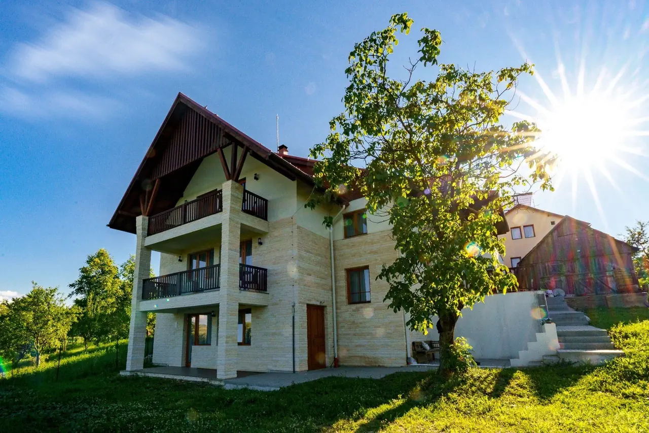 Pensiunea Szentkirály din Sâncraiu, văzută din grădină: patru niveluri, balcoane de lemn și un nuc în soare